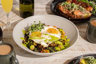 A vibrant bowl of sautéed greens topped with two sunny-side-up eggs, drizzled with sauce, surrounded by drinks and additional dishes.
