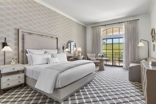 A stylish, modern bedroom features a king-sized bed, cozy seating, and large windows, creating an inviting atmosphere with soft tones.