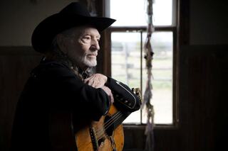 A weathered musician with a guitar gazes thoughtfully out a window, embodying the spirit of classic country music.