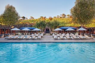 A serene pool area features lounge chairs and umbrellas, set against a backdrop of greenery and elegant arches. Perfect for relaxation.
