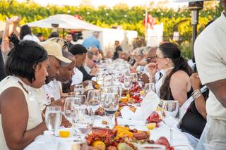 Guests enjoy a lively outdoor seafood feast at a long table, adorned with crawfish, corn, and drinks in a festive atmosphere.