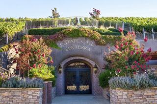 A couple relaxes by a serene poolside, enjoying refreshments under sunshades, with lush vineyards in the background.