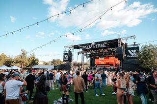 A lively outdoor festival scene with people dancing joyfully, dressed in colorful outfits under a sunny sky. Fun and energy fill the air.