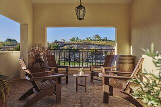 A cozy patio features wooden chairs arranged around a small table, with a view of greenery and gentle hills beyond the railing.