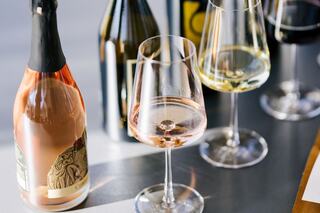 A rose wine bottle stands next to glasses of white and red wine, showcasing a sleek and elegant tasting setup.