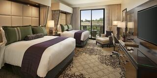 A cozy hotel room features two beds, elegant decor, a TV, and a balcony with scenic views, creating a welcoming atmosphere.