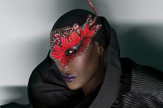 A striking figure adorned with a dramatic red butterfly mask and dark attire, exuding elegance and mystique.