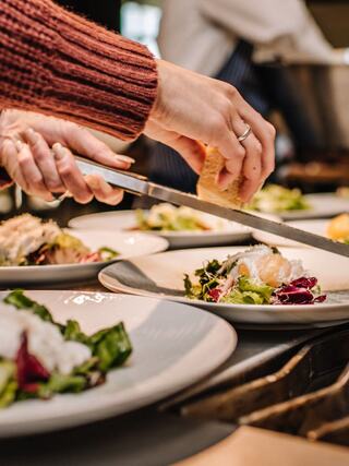 A hand delicately garnishes plates of colorful salad and seafood, showcasing culinary preparation in a fine dining setting.