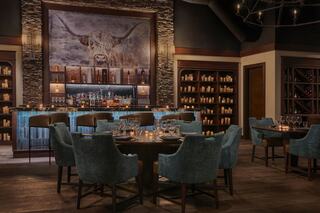 A cozy restaurant features elegant seating, a striking bar with a well-stocked display, and rustic decor highlighted by a large mural.