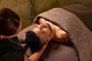 A man enjoys a relaxing massage while lying on a treatment table, covered with a blanket, in a serene spa setting.