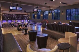 A stylish bowling alley features lounge seating, modern decor, and illuminated lanes, creating a vibrant and inviting atmosphere.