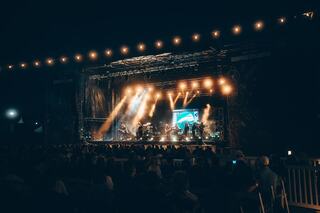 A lively outdoor concert features illuminated musicians on stage, with a captivated audience enjoying the nighttime atmosphere.