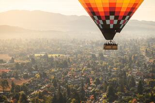 A vibrant hot air balloon glides over a picturesque landscape of hills and colorful autumn trees, illuminating the tranquil morning sky.