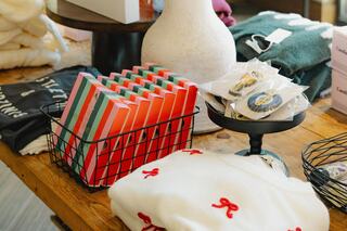 A cozy display features colorful notebooks in a basket, cookies on a stand, and a cozy sweater with cute embroidery on a wooden table.