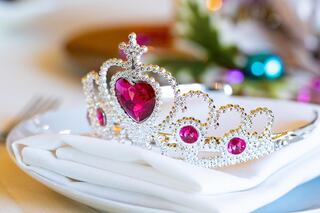 A sparkling tiara adorned with pink gems rests elegantly on a white napkin, hinting at a festive celebration or royal theme.