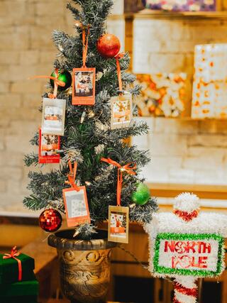 A festive mini Christmas tree adorned with polaroid photos, colorful ornaments, and a cheerful sign reading "North Pole." Gifts await underneath.