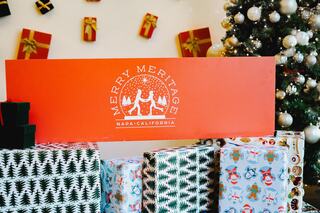 A festive scene with wrapped gifts, a decorated tree, and a cheerful sign reading "Merry Meritage Napa, California." Holiday spirit abounds!