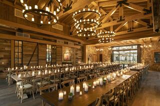 A spacious, rustic dining hall with wooden beams, large tables, and candlelight creates a warm, inviting atmosphere perfect for gatherings.