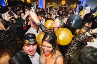 A lively New Year's Eve celebration with a crowd wearing festive attire, balloons, and joyful expressions, capturing the excitement of the moment.