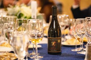 A bottle of Trinitas wine stands proudly on a beautifully set dining table, surrounded by elegant glassware and plates of food.