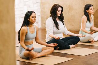 Three women meditate on yoga mats in a serene setting, focusing inward and cultivating a sense of peace and mindfulness.