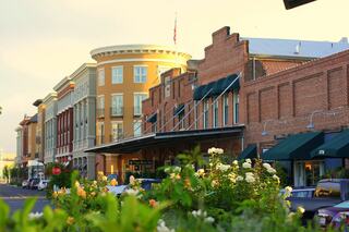 A picturesque street lined with charming buildings, featuring a mix of brick and modern architecture, vibrant flowers, and parked cars.
