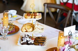 A beautifully arranged tiered platter displaying an assortment of pastries, cookies, and sandwiches, set on an elegant dining table.