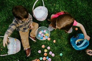 Two kids search for colorful Easter eggs on the grass, surrounded by baskets filled with hidden treasures. Joyful, festive atmosphere.