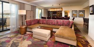 A spacious, stylish living area features a plush sectional sofa, a coffee table, and colorful rugs, complemented by elegant lighting and decor.