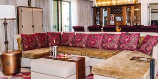 A stylish hotel room lounge area features a large sectional sofa with vibrant pillows, a chic coffee table, and modern decor elements.