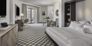 A stylish luxury hotel room featuring a cozy bed, elegant furnishings, and a neat sitting area with natural light streaming in.