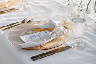 A beautifully set table features an elegant plate with a menu, a folded napkin, glassware, and name card, all adorned in soft lighting.
