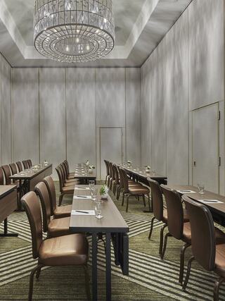 A modern meeting room features elegant lighting, rows of tables, and chairs, with a stylish carpet and a sophisticated ambiance.