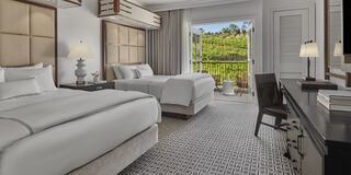 A stylish luxury hotel room features a king-sized bed, elegant decor, a work area, and large windows, overlooking vineyards creating a bright and inviting atmosphere.