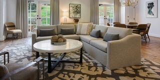 A stylish living area features a large sectional sofa, a round coffee table, and elegant decor, with natural light coming through large windows.