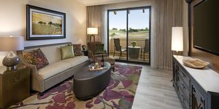 A cozy living area features a sofa, decorative pillows, a stylish rug, and a large window with a view of a balcony and outdoor scenery.