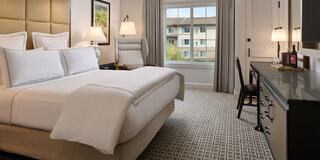 A cozy hotel room featuring a plush bed, stylish furniture, and large windows showcasing an outdoor view. Warm, inviting decor throughout.