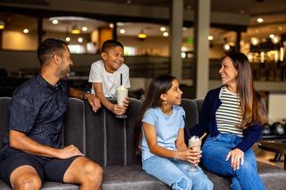 A family enjoys milkshakes while sharing smiles and laughter in a cozy, modern café setting.