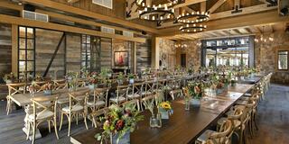 A spacious, elegantly decorated dining area features long wooden tables adorned with vibrant floral arrangements and rustic chandeliers.