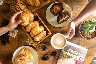 Croissants, muffins, and a latte on a rustic wooden table, complemented by a book and a succulent plant, creating a cozy café vibe.