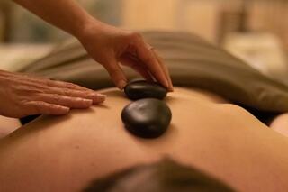 A person receives a hot stone massage, with smooth stones placed on their back while a therapist gently assists.