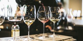 A red wine is being poured into a glass alongside two empty wine glasses, set against a blurred background.