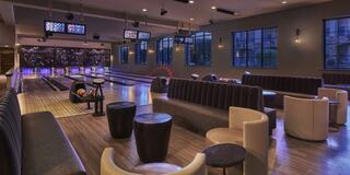 A modern bowling alley features cozy seating, stylish decor, and bright lights, creating a welcoming atmosphere for socializing and fun.