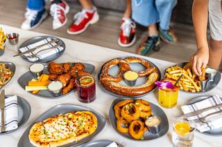 A spread of delicious appetizers including wings, pretzels, pizza, and fries, accompanied by colorful drinks, awaits eager diners.