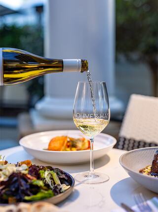 A glass at Olive & Hay is filled with white wine, alongside two dishes: a salad and a seafood entrée, set in a cozy dining atmosphere.