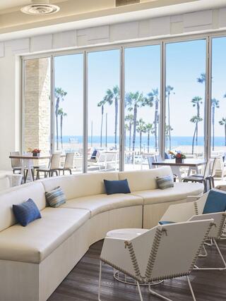 Bright, modern coastal lounge with curved seating, ocean views, and palm trees. Light and airy atmosphere perfect for relaxation.