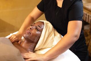 A person receives a relaxing facial treatment while lying down, with a professional gently massaging their shoulders.