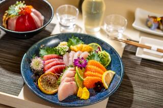 A beautifully arranged platter of fresh sashimi, garnished with colorful herbs and citrus, complemented by sake and elegant tableware.