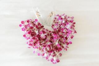 A heart-shaped arrangement of vibrant pink orchids adorned with delicate ribbons, symbolizing love and elegance.
