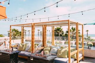 Cozy lounge area with wooden cabanas, colorful cushions, and ocean views, adorned with string lights for a relaxed, stylish vibe.